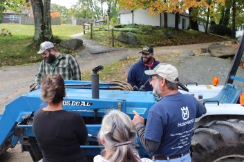 A small group stands around a blue, Ford tractor.